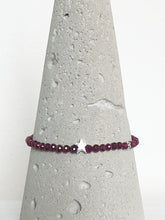 Lade das Bild in den Galerie-Viewer, Klassisch-dezentes Armband aus facettiertem rotem Granat und einem mattierten Stern aus Echtsilber, begleitet von einem zierlichen Silberblümchen, Detailansicht auf Betonkegel.