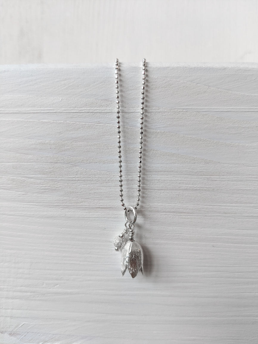 Silberkette mit einem schicken Ensemble aus eine stilisierten Blüte mit einem kleinen kugelförmigen Begleiter. Hier bequem online kaufen.
